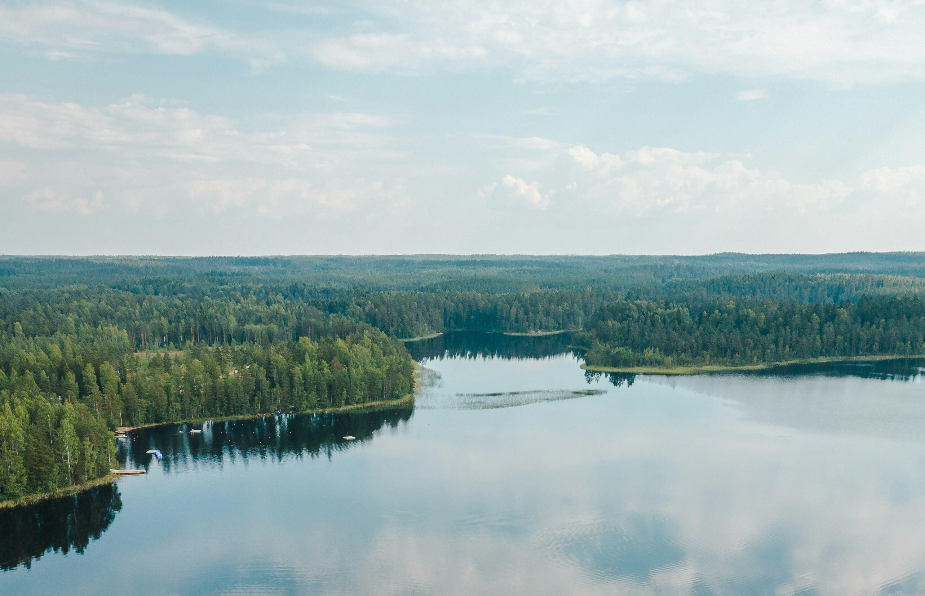 A picturesque view of Lake Saimaa in Finland: the purest and the deepest water surface surrounded by dense forest, reflecting the blue sky with clouds.